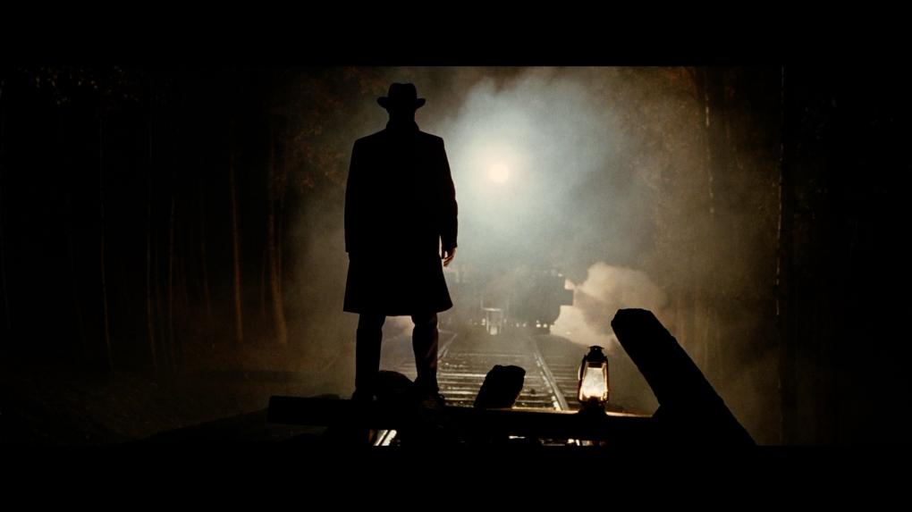 Jesse James steht auf einer auf den Gleisen erbauten Barrikade. Ein Zug nähert sich.