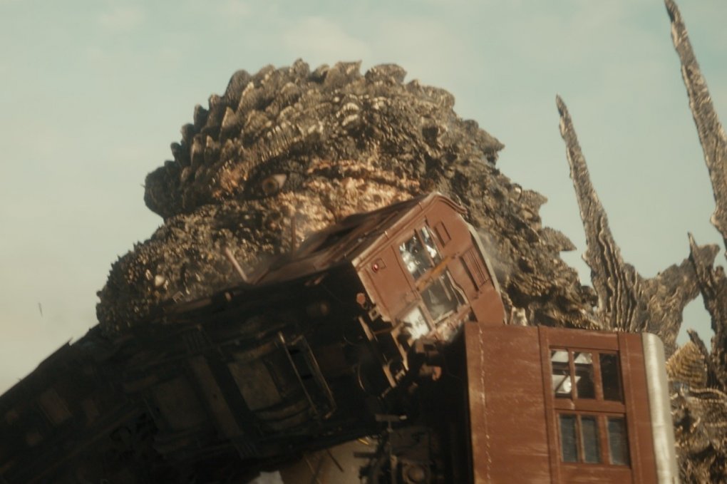 Godzilla im neuen Kinofilm Godzilla Minus One, der einen Bahn-Waggon in seinem Maul hat