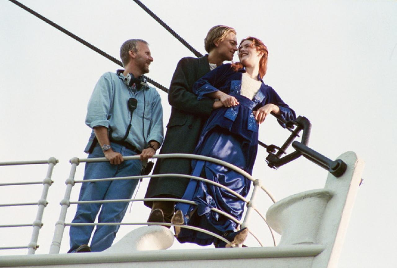 James Cameron steht mit Leonardo DiCaprio und Kate Winslet am Bug der Titanic.