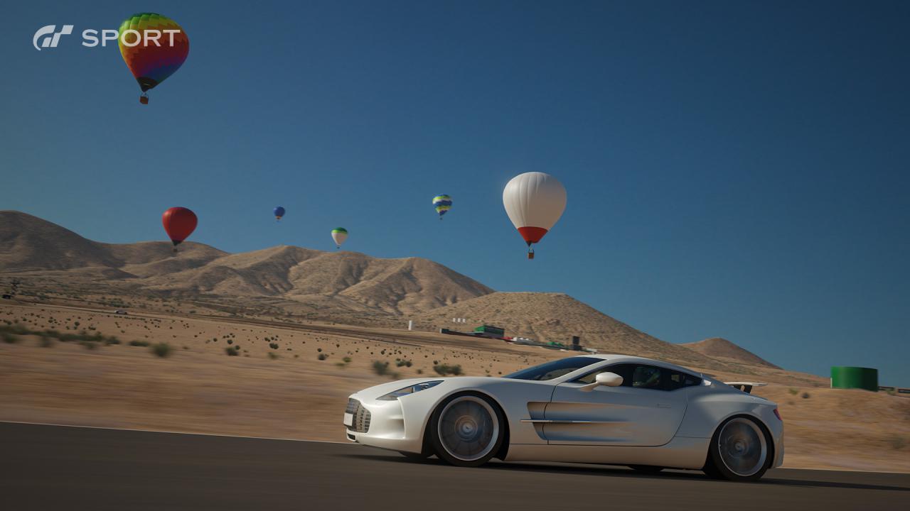 Ein Auto fährt durch die Wüste, im Hintergrund Heißluftballons.