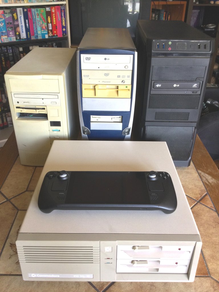 [20/09/2022] Vier Rechner und ein Handheld: Ganz vorne steht der PC-10 III von Commodore, der technisch einem IBM Personal Computer XT oder einem kleinen 286er ebenbürtig war. Dahinter seht ihr von links nach rechts jeweils einen Tower aus den 1990er-, 2000er- und 2010er-Jahren, während auf dem Desktop-Gehäuse das neue Steam Deck liegt.