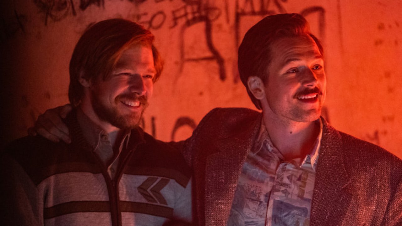 Henk Rogers (Taron Egerton) und Alexei Paschitnow (Nikita Efremov), die lachend in rotem Licht Arm in Arm gezeigt werden.