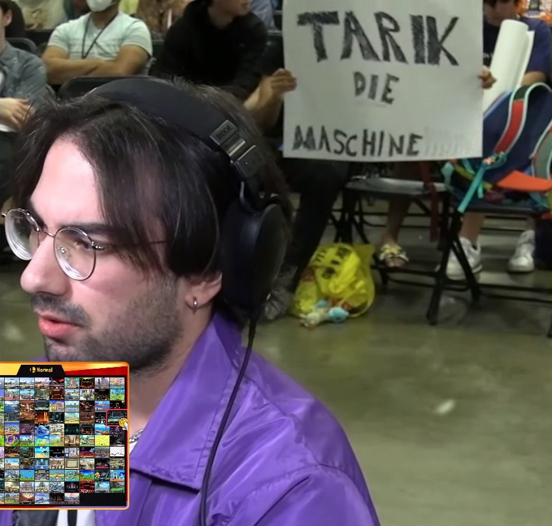 Smash-Turnierspieler Tarik. Im Hintergrund hält jemand ein Schild hoch, auf dem "Tarik die Maschine" steht.