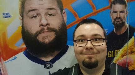 Die Schlange für ein Treffen mit Kevin Owens bei Axxess war so lang, dass sich Chris für ein Selfie mit einer Posterwand entscheidet. So ist wenigsten noch Bobby Roode mit drauf.