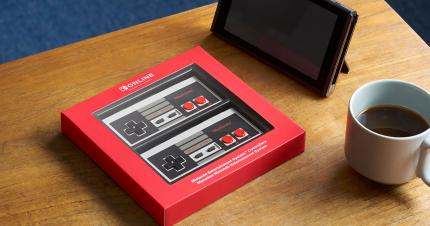 Auf dem Bild ist ein Tisch mit einer Tasse Kaffee, einer Nintendo Switch im Tisch-Modus sowie einer Packung mit zwei neu aufgelegten NES-Controllern zu sehen.